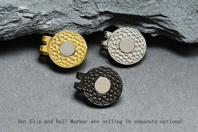May include: Three golf ball markers, one gold, one silver, and one black, with a textured surface and a smooth, round center.  Hat Clip and Ball Marker are selling in separate options!