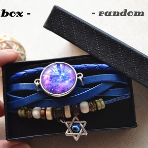 May include: A blue leather bracelet with a galaxy charm and an evil eye charm. The bracelet is in a black gift box. "Gift box - random color" is written on the box.