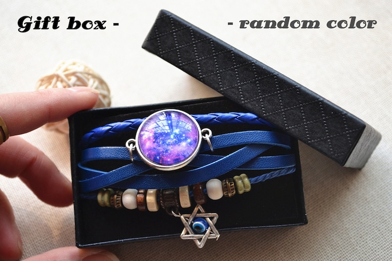 May include: A blue leather bracelet with a galaxy charm and an evil eye charm. The bracelet is in a black gift box. "Gift box - random color" is written on the box.