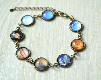 May include: A bronze chain bracelet with eight round glass charms featuring images of planets from the solar system. The planets include Earth, Mars, Jupiter, Saturn, Uranus, Neptune, Venus, and Mercury.
