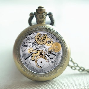 May include: A round antique brass pocket watch with an intricate engraved border and a visible mechanical movement. The internal clockwork features exposed silver and gold-toned gears, springs, and levers, with a winding crown at the top.
