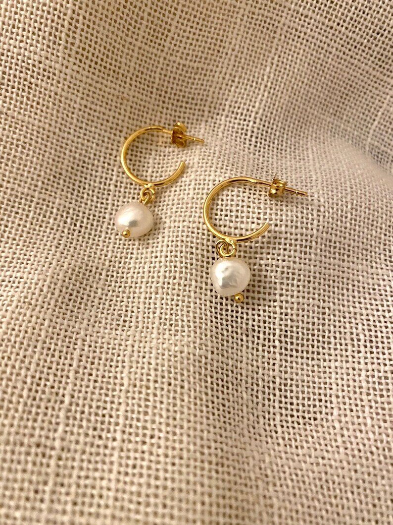 May include: A pair of gold hoop earrings with a single white pearl dangling from each hoop.
