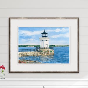 Large framed watercolor art print of Bug Light styled above a mantel, highlighting the South Portland lighthouse and sparkling harbor.