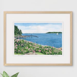 Framed watercolor art print of Spruce Point staged in a bright interior, featuring blooming roses and ocean view in Boothbay Harbor.