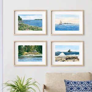 May include: Four framed watercolor paintings of seascapes. The top left painting shows a rocky coastline with a pier and a sailboat in the distance. The top right painting shows a sailboat sailing on a calm blue sea. The bottom left painting shows a small house on a wooded island with a waterfall in the foreground. The bottom right painting shows a rocky coastline with a large wave crashing against the rocks.