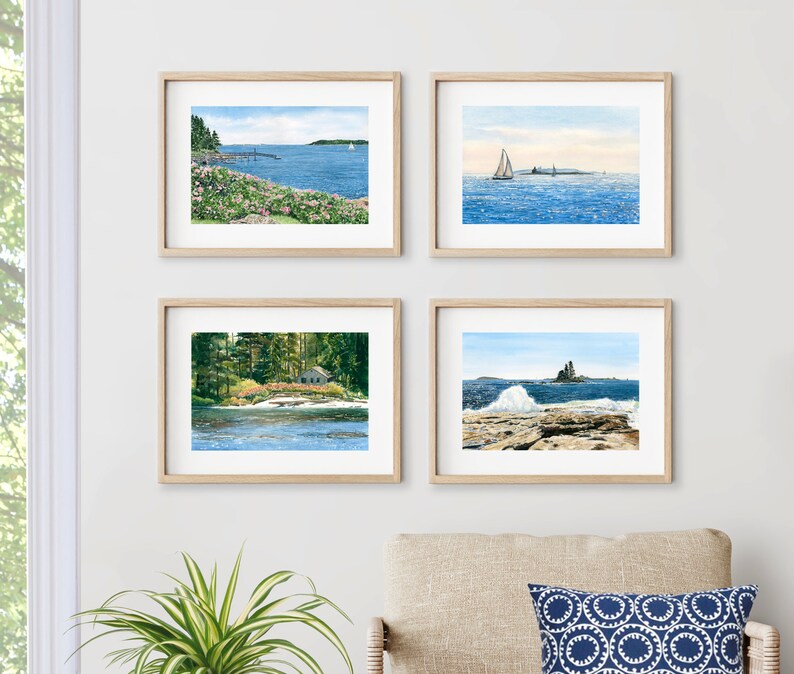 May include: Four framed watercolor paintings of seascapes. The top left painting shows a rocky coastline with a pier and a sailboat in the distance. The top right painting shows a sailboat sailing on a calm blue sea. The bottom left painting shows a small house on a wooded island with a waterfall in the foreground. The bottom right painting shows a rocky coastline with a large wave crashing against the rocks.