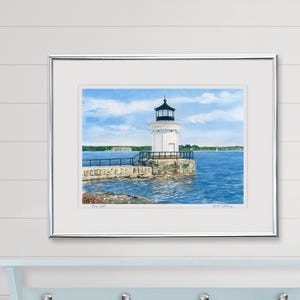 Framed watercolor art print of Bug Light displayed in a coastal-inspired room, featuring the lighthouse and Fort Gorges beyond.