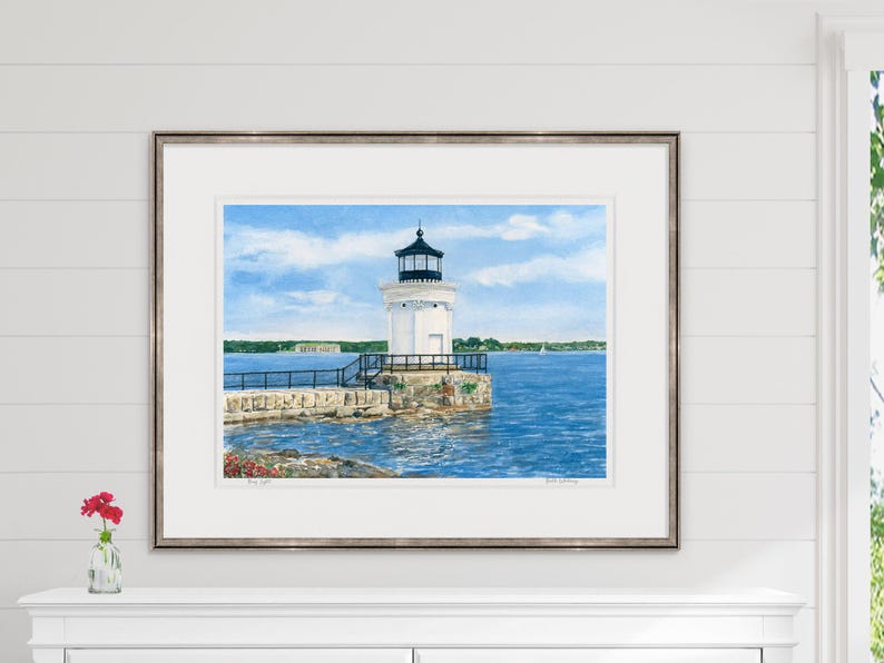 Large framed watercolor art print of Bug Light styled above a mantel, highlighting the South Portland lighthouse and sparkling harbor.