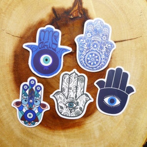 May include: Five blue and white hamsa hand stickers with an evil eye design. The hamsa hands are decorated with different patterns, including floral, geometric, and text.