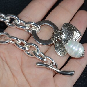 Puede incluir: Un brazalete de cadena de plata con un dije de coraz&oacute;n, un dije de perla y un dije con las palabras "Vive Espana".