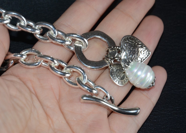 Puede incluir: Un brazalete de cadena de plata con un dije de coraz&oacute;n, un dije de perla y un dije con las palabras "Vive Espana".