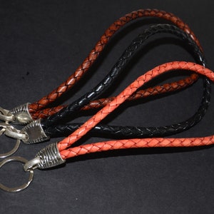 Op de afbeelding: Drie gevlochten leren sleutelhangers in oranje, bruin en zwart met zilveren sleutelringen.