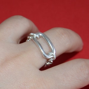 Puede incluir: Un anillo de plata con un gran diseño de eslabón ovalado. El anillo se lleva en un dedo.