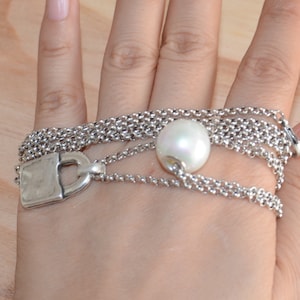 May include: A silver chain bracelet featuring a padlock charm and a white pearl. The bracelet is layered and has a delicate design.