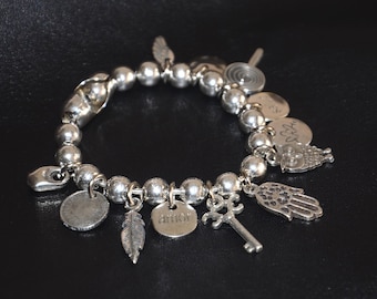 Puede incluir: Un brazalete de plata con una variedad de dijes, incluyendo una pluma, una llave, una mano, un búho y un corazón con la palabra "amor" en él.