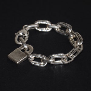 Op de afbeelding: Een zilveren kettingarmband met een hangslot sluiting. De ketting is gemaakt van ovale schakels met een getextureerd oppervlak.