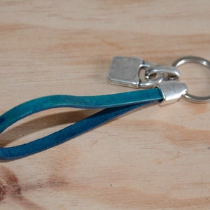 May include: A teal blue leather keychain with a silver key ring and a silver clasp.
