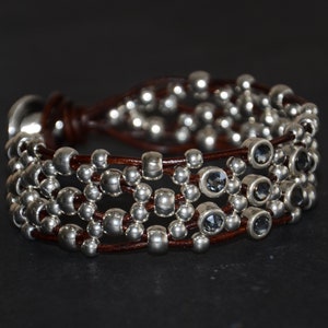 May include: A brown leather bracelet with multiple strands of silver beads and dark gray faceted stones.