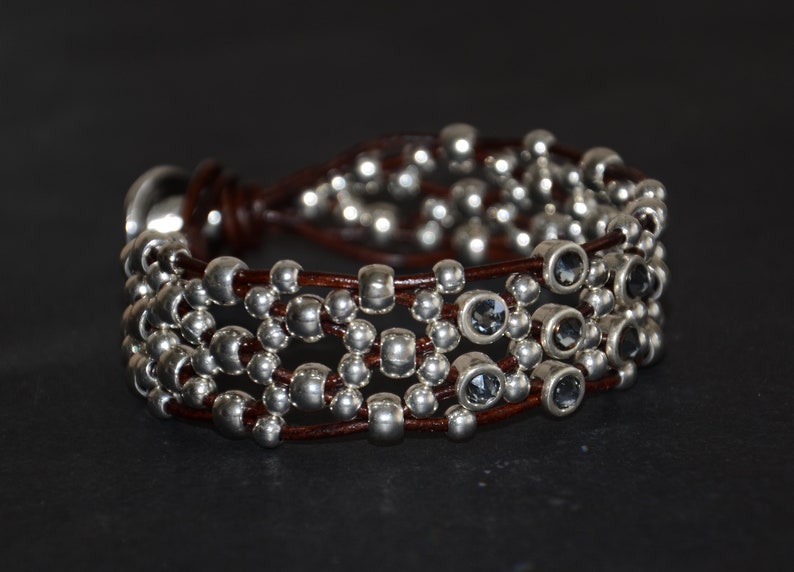 May include: A brown leather bracelet with multiple strands of silver beads and dark gray faceted stones.
