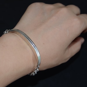 May include: A silver bracelet with a flat, curved bar and a chain of small beads.