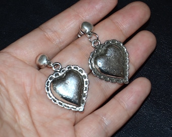May include: A pair of silver heart-shaped earrings with a textured design. The earrings are hanging from a silver chain.