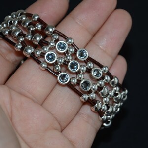 May include: A multi-strand bracelet with brown leather cords and silver beads interspersed with dark blue gemstones.