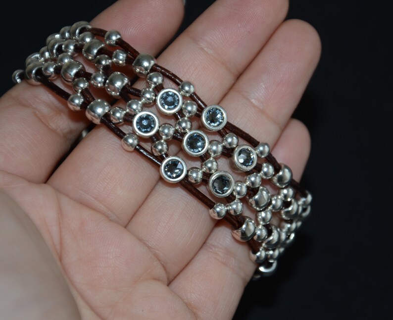 May include: A multi-strand bracelet with brown leather cords and silver beads interspersed with dark blue gemstones.