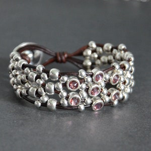 May include: A brown leather bracelet with multiple strands of silver beads and pink gemstones.