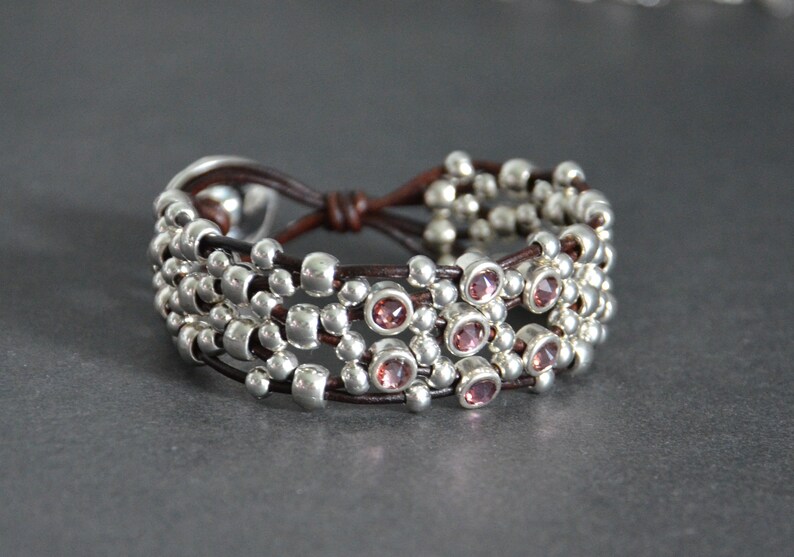 May include: A brown leather bracelet with multiple strands of silver beads and pink gemstones.