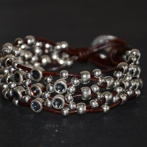 May include: A brown leather bracelet with multiple strands of silver beads and dark blue crystal accents.