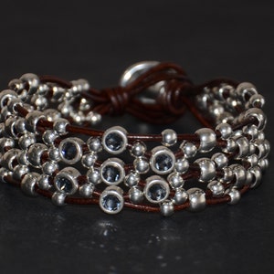 May include: A brown leather bracelet with multiple strands of silver beads and blue gemstone accents.