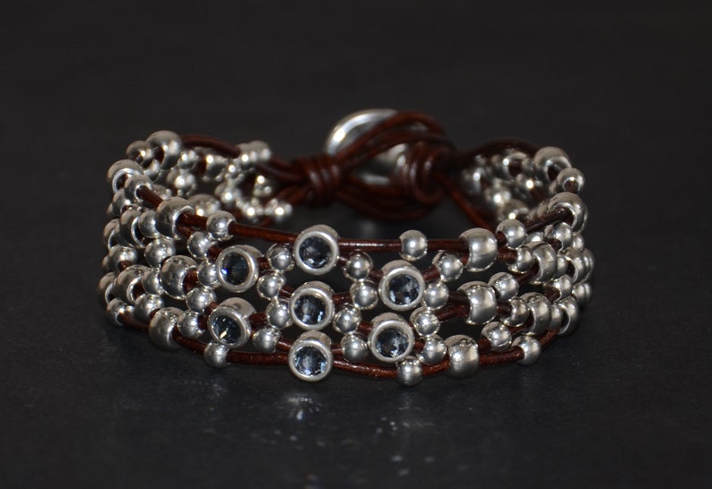 May include: A brown leather bracelet with multiple strands of silver beads and blue gemstone accents.