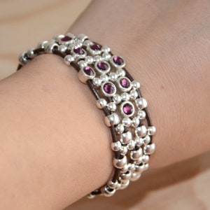 May include: A multi-strand bracelet with brown leather cord and silver beads accented with purple gemstones.