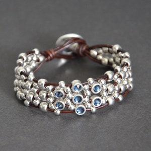 May include: A brown leather bracelet with silver beads and blue gemstones. The bracelet is adjustable with a sliding knot.