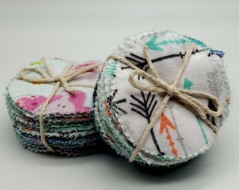 May include: Two stacks of reusable cotton rounds, each tied with twine. One stack features a colorful animal print, the other has a black and white arrow print.