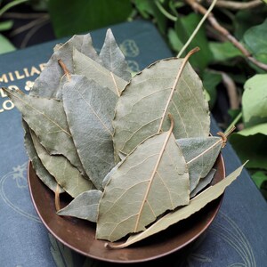 May include: A small copper bowl filled with dried bay leaves. The bowl is sitting on a green book with a floral design.