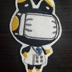 May include: Embroidered iron-on patch featuring a cartoon character wearing a white lab coat, a blue tie, and a white face mask with black accents. The character has black ears and gold accents on the ears and shoulders.