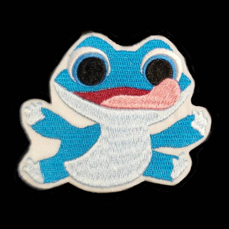 Pu&ograve; includere: Una toppa ricamata con una rana dei cartoni animati con un grande sorriso e la lingua che sporge, in blu e bianco.