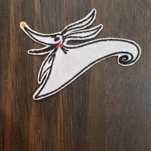 Op de afbeelding: Witte geborduurde strijkpatch van Zero, de spookhond uit The Nightmare Before Christmas, met zwarte stiksels en een rode mond.