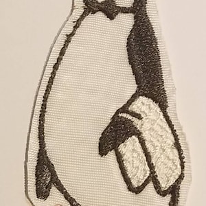 May include: A white embroidered penguin with black and orange details. The penguin is standing with its wings folded and its head tilted to the side.