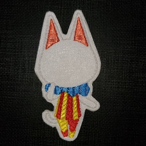 Op de afbeelding: Witte geborduurde patch van een cartoonkat met een blauw-witte strik en een rood-gele gestreepte broek.