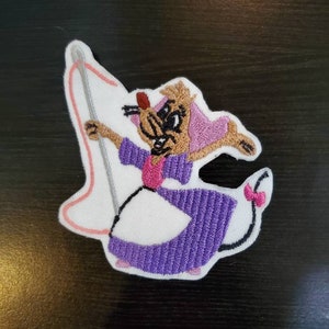 May include: An embroidered patch featuring a cartoon mouse holding a needle and thread. The mouse is wearing a purple dress and a pink bow. The patch is white with pink and purple stitching.