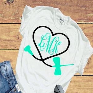 May include: White t-shirt with a black stethoscope in the shape of a heart. The heart has the monogram "LMK" in a teal color.