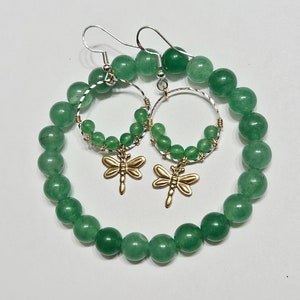 Peut inclure: Un ensemble de bijoux en perles vertes, comprenant un bracelet et des boucles d'oreilles. Les boucles d'oreilles ont des cerceaux argentés avec des breloques dorées en forme de libellule. Le bracelet et les boucles d'oreilles sont faits de perles vertes rondes.