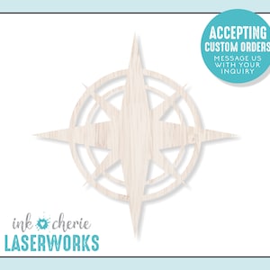 May include: A wooden compass rose cut-out with a light wood grain finish. The design features four main points and a circular inner design. The text "Accepting Custom Orders" is in a teal circle. The logo "ink cherie LASERWORKS" is at the bottom.