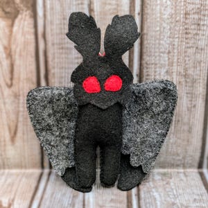 May include: A black felt moth with red eyes and gray wings. The moth is a handmade toy.