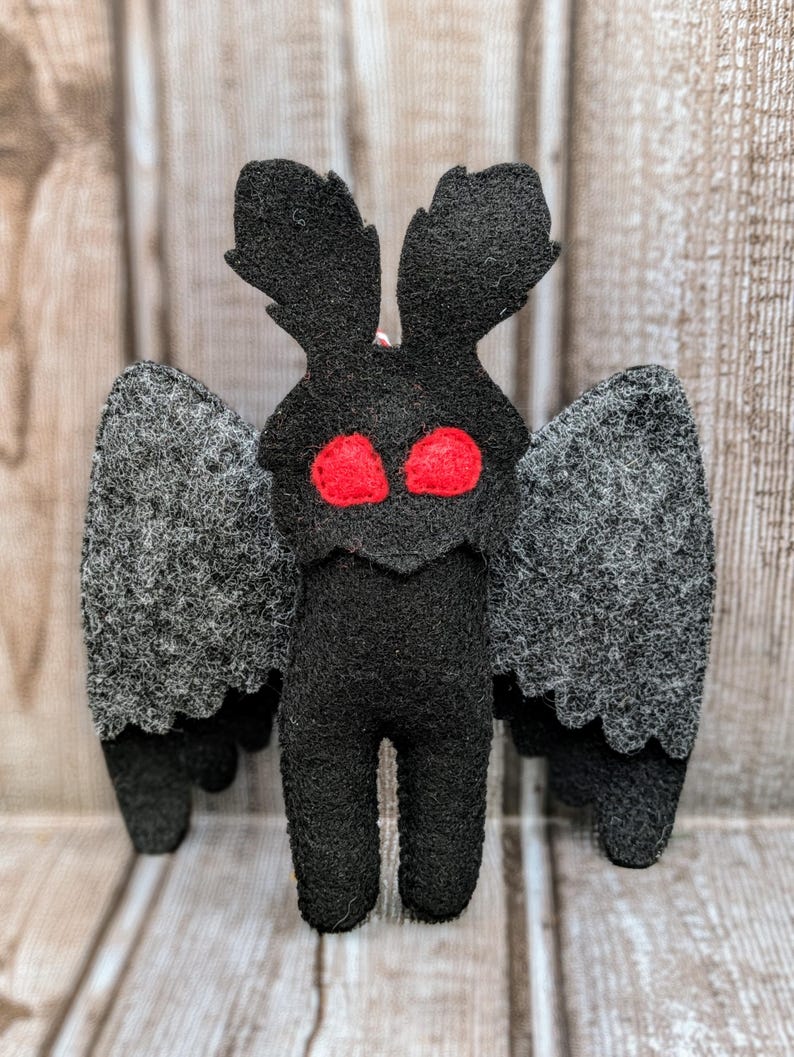May include: A black felt plush toy shaped like a moth with large red eyes and gray wings.