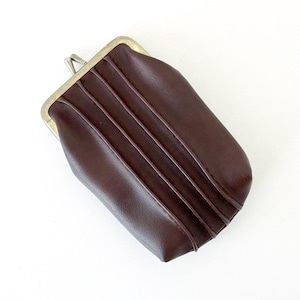 May include: A dark brown rectangular coin purse featuring a metallic kiss-lock closure at the top. The exterior surface of the purse is smooth and accented with three vertical stitched pleats running down the front face of the item.