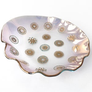 May include: A decorative, iridescent glass dish with a scalloped edge and gold trim. The dish features a pattern of gold and teal circular and starburst designs. The dish is approximately 10 inches in diameter.