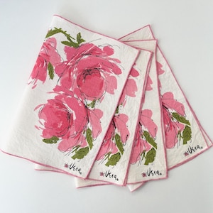 May include: Set of four white linen napkins with a pink rose floral design. Each napkin features a pink border and the signature "Vera" in black script. The roses are painted in shades of pink with green leaves.
